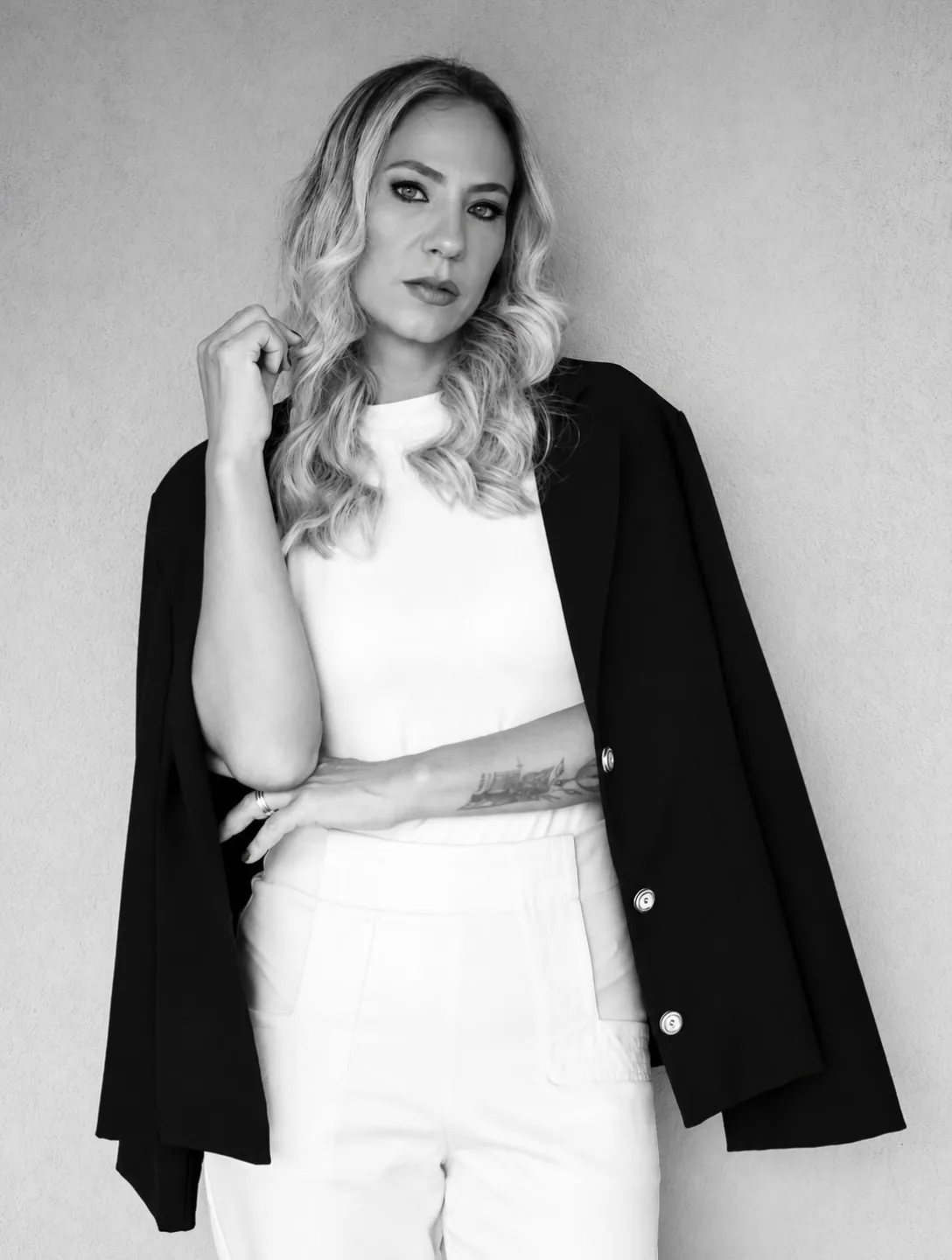 Mulher com blazer preto e lingerie branca diante de fundo claro