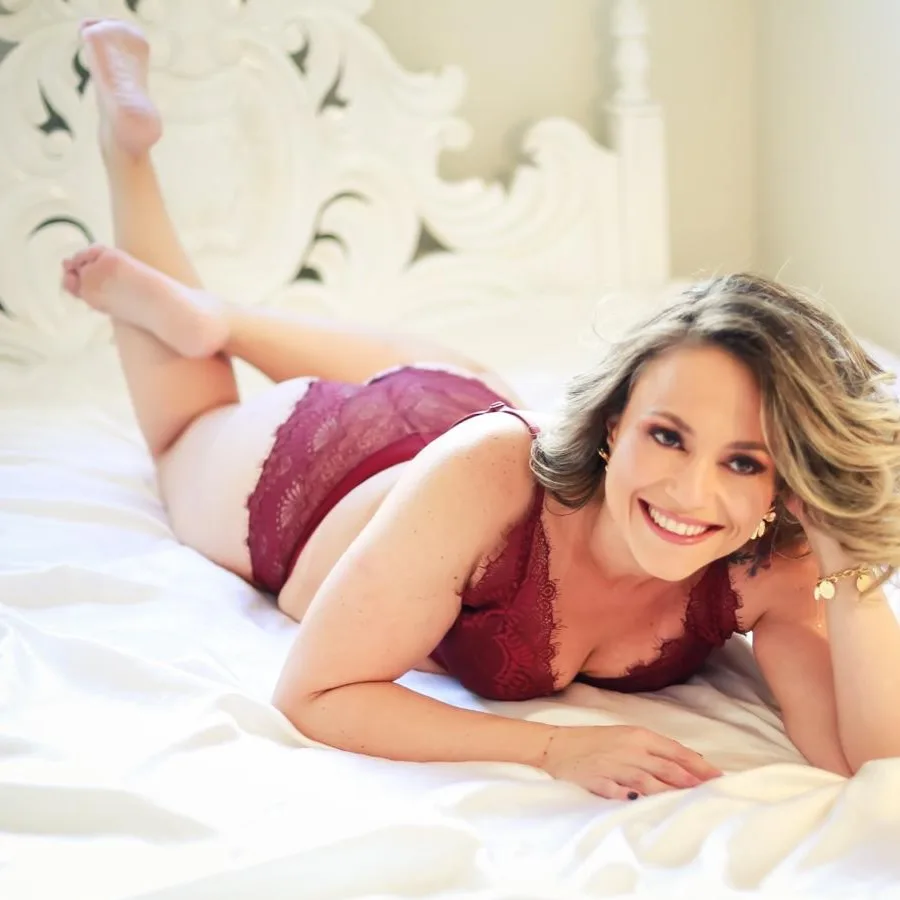 Mulher sorrindo deitada na cama, com lingerie vinho