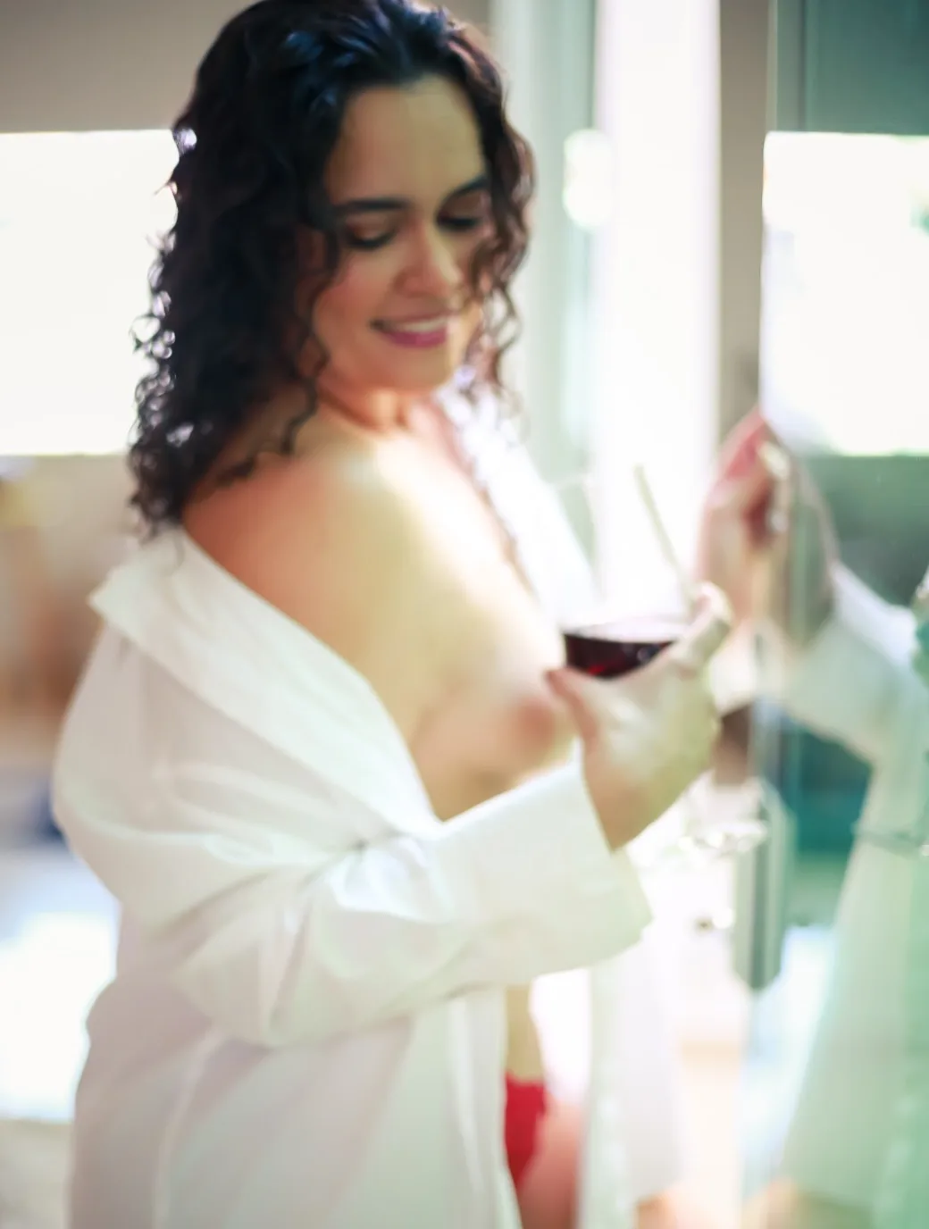 Mulher com camisa branca junto a uma janela de moldura verde