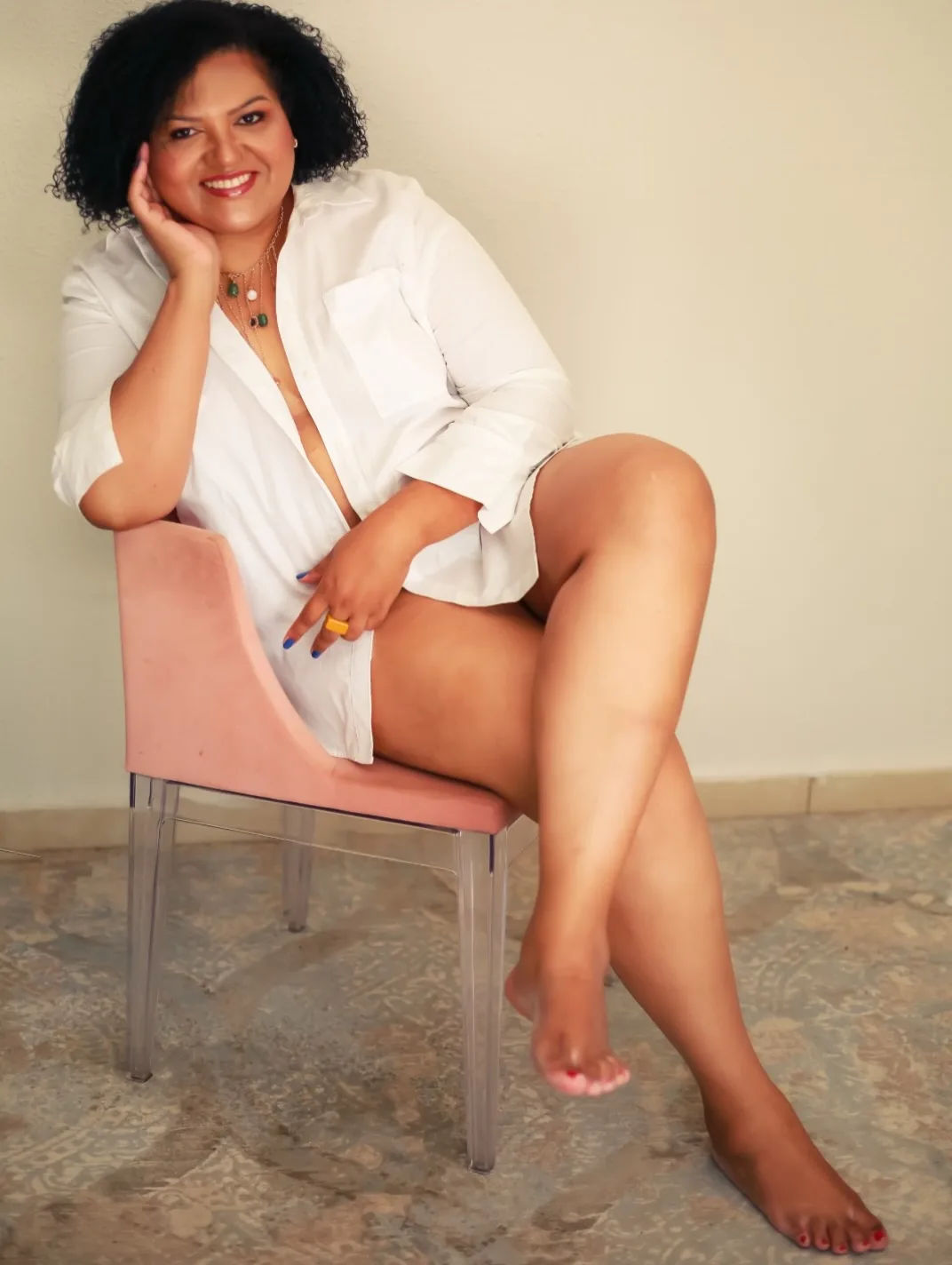 Mulher sentada em poltrona rosada, usando camisa branca