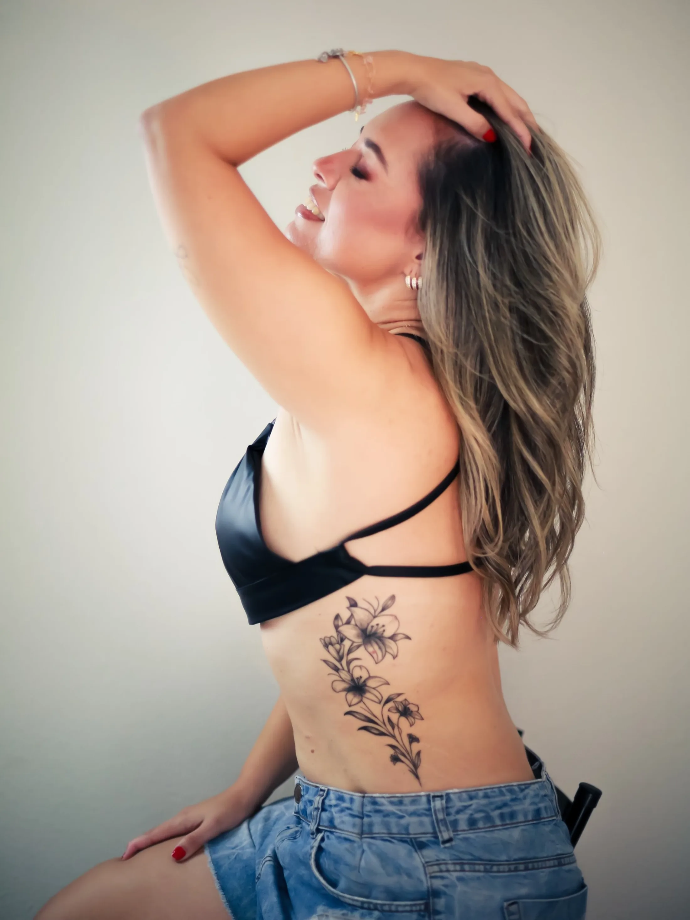 Mulher com lingerie preta e calça jeans, com um braço acima da cabeça