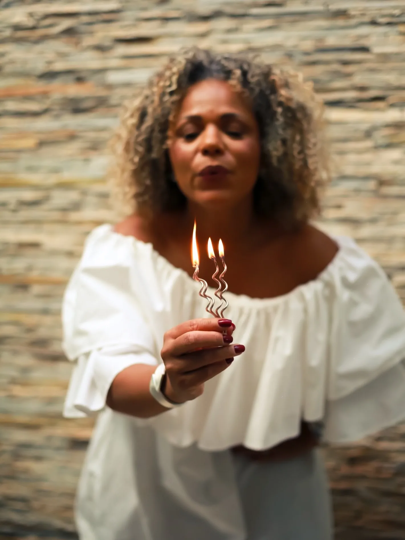 Mulher com blusa branca segurando um pequeno bolo com velas