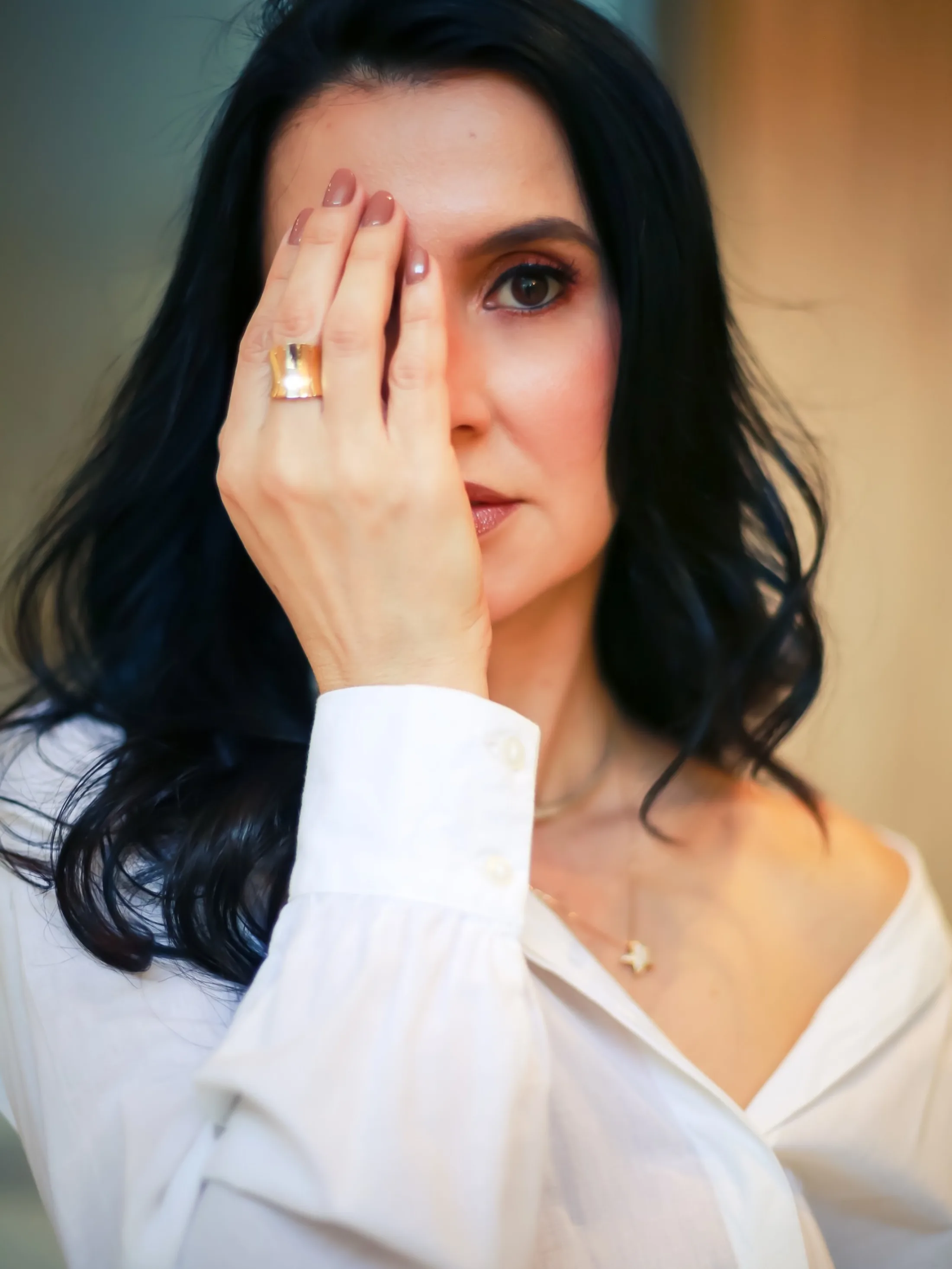 Mulher com camisa branca e uma das mãos diante de um olho