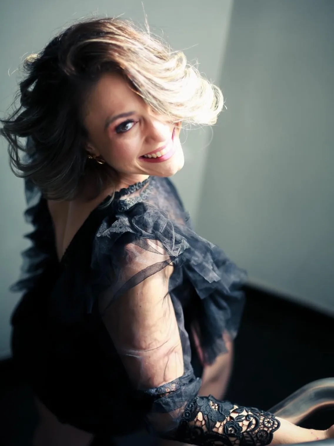 Mulher com roupa preta de renda junto à janela