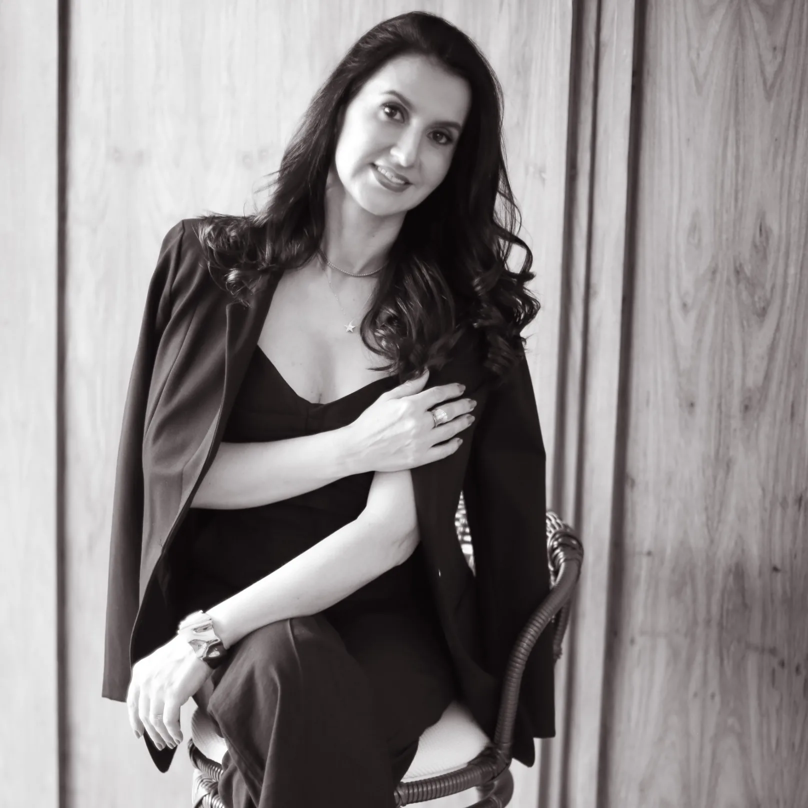 Mulher de blazer preto e lingerie branca junto à cortina, em preto e branco